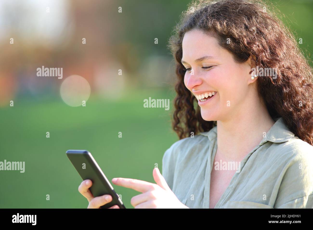 Donna felice che cammina in un parco controllare smartphone Foto Stock
