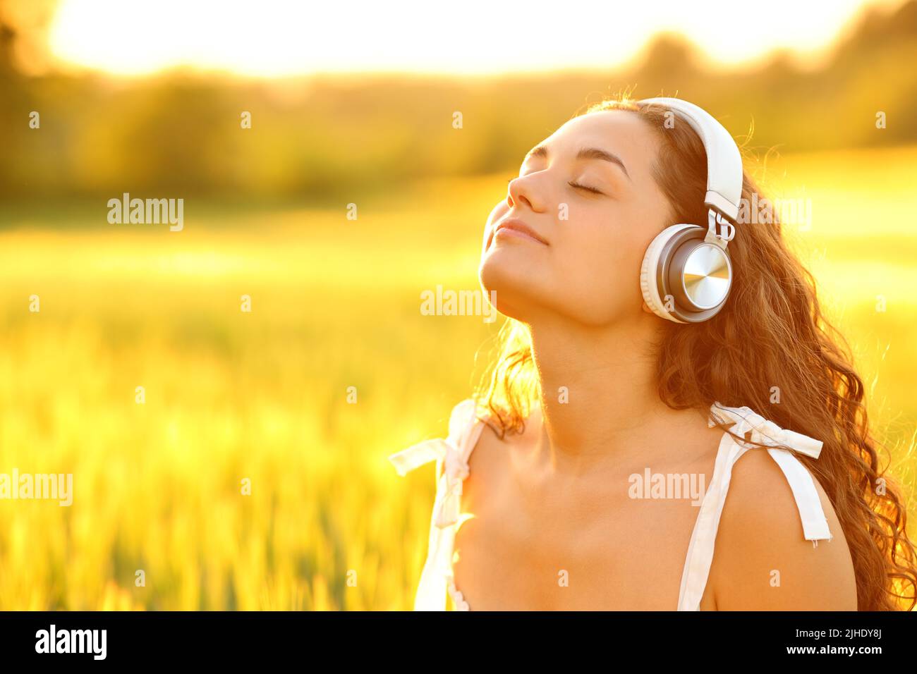 Donna rilassata meditando con cuffie wireless in un campo di grano al tramonto Foto Stock