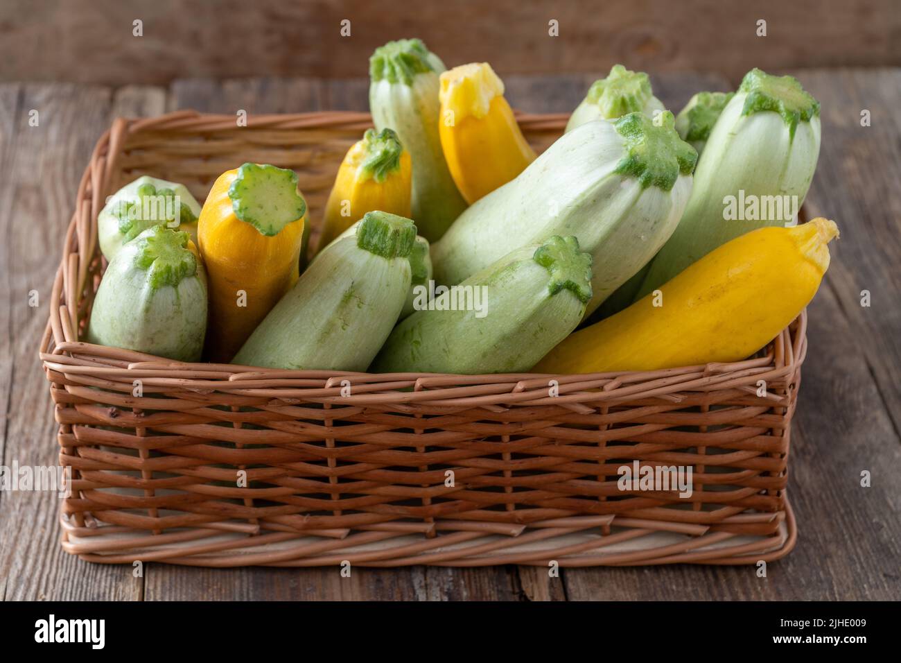 Zucchine multicolore gialle, verdi, bianche, arancioni sul tavolo in legno in primo piano. Sfondo alimentare. Zucchine fresche raccolte in cestino, zucca estiva tagliata. Zucchine verdi selezionate. Foto Stock