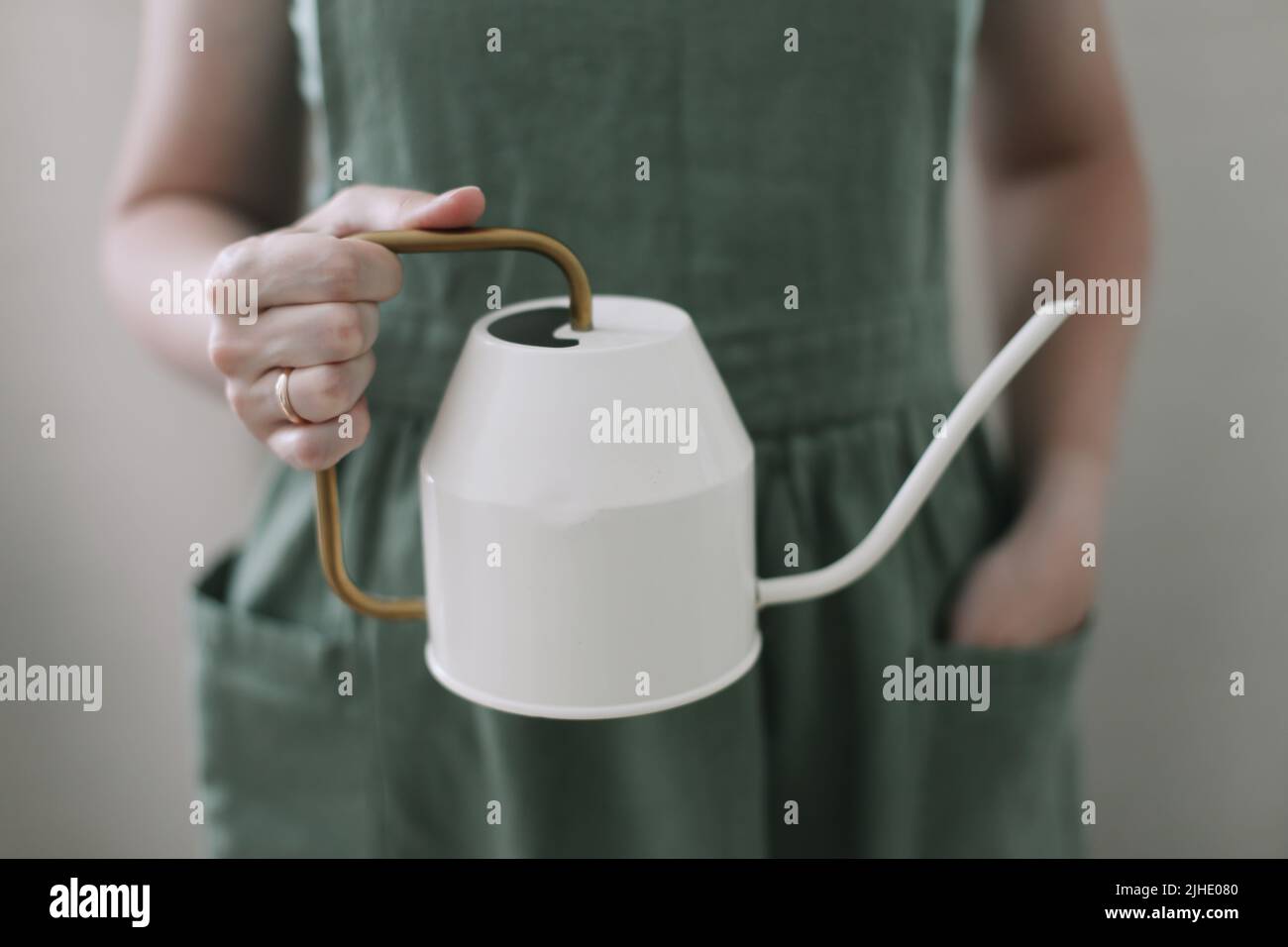 Ragazza in grembiule tiene un annaffiatoio. Annaffiatura e cura di piante domestiche. Giardinaggio domestico. Coltivazione di fiori di hobby Foto Stock