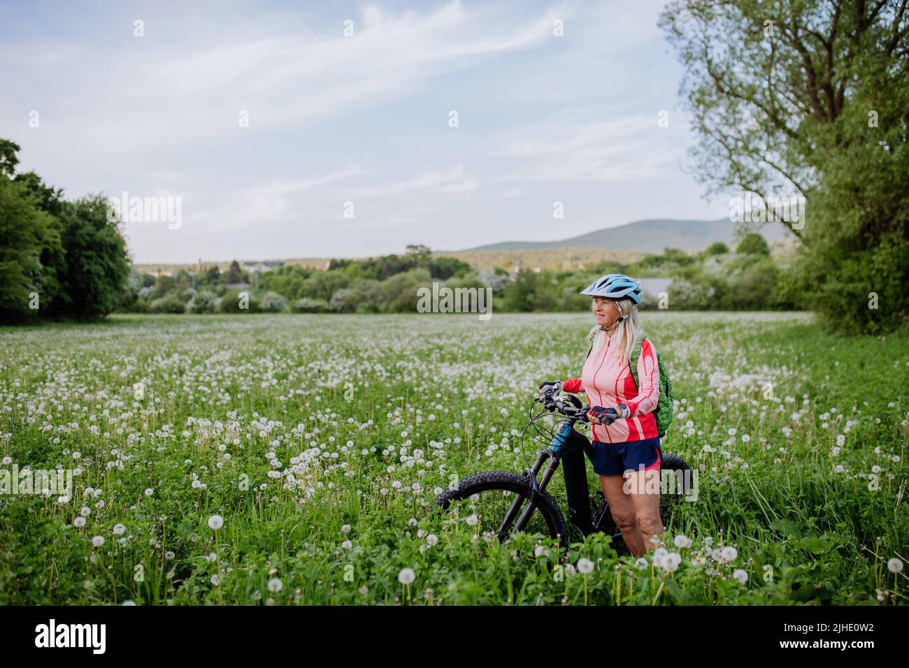 Donna anziana attiva con bicicletta elettrica sul prato in estate, concetto di stile di vita sano. Foto Stock