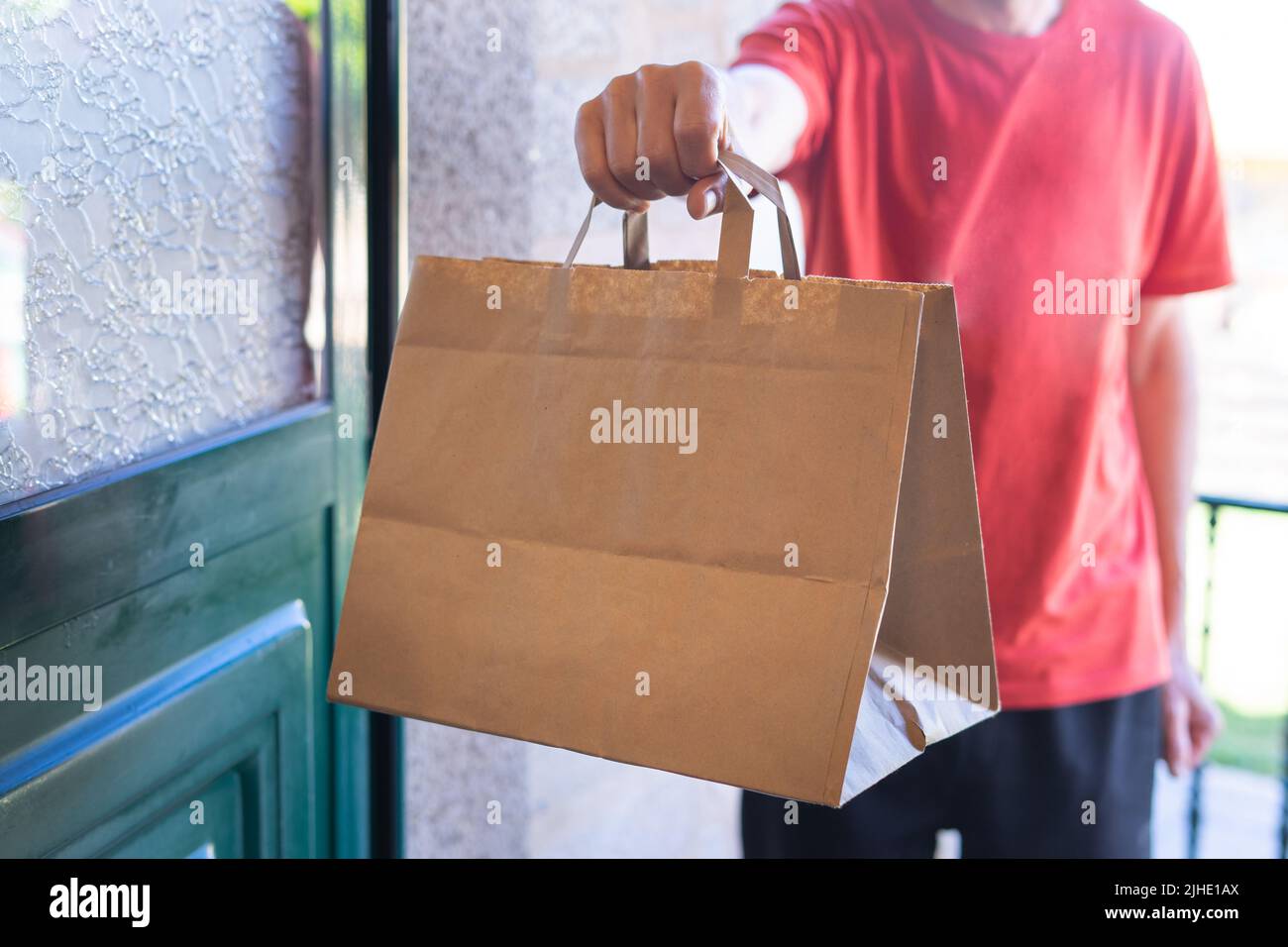 Uomo che consegna un sacchetto di carta alla porta anteriore. Shopping online. Consegna a domicilio. Foto Stock