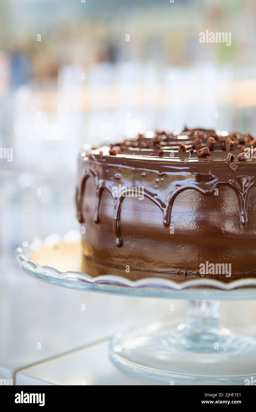 Torta al cioccolato dall'aspetto delizioso con glassa di ganache e decorata semplicemente con scaglie di cioccolato fondente visualizzate su un supporto di vetro Foto Stock