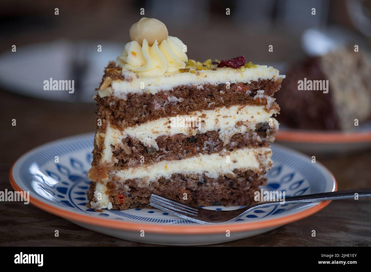 Fetta di gustoso dolce a tre strati di carote dolci e umide farcite di noci pecan tostate e deliziosa glassa di formaggio cremoso servita su un piatto di ceramica Foto Stock