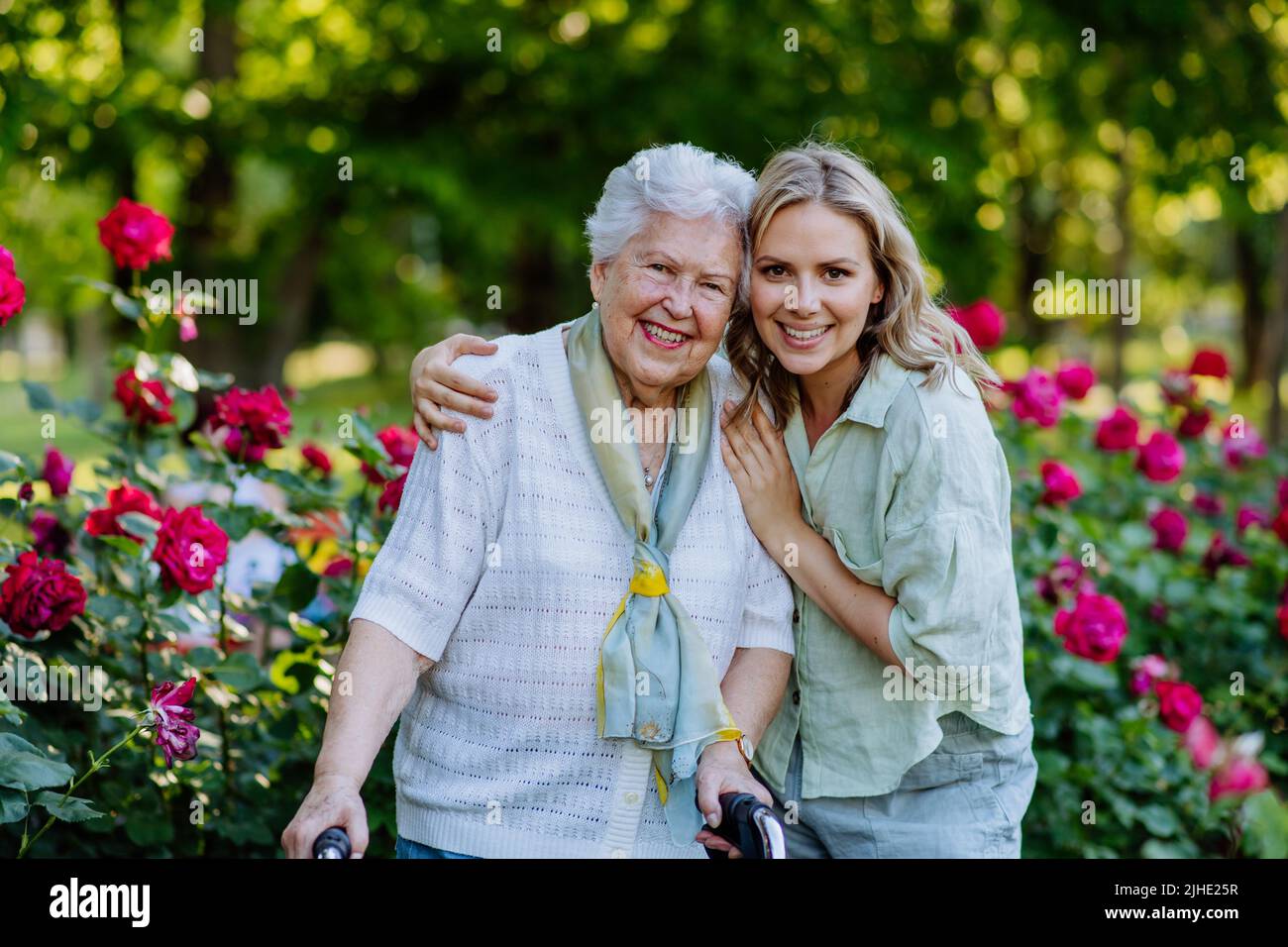 Ritratto di nipote adulto con nonna anziana a piedi nel parco, con rose sullo sfondo Foto Stock