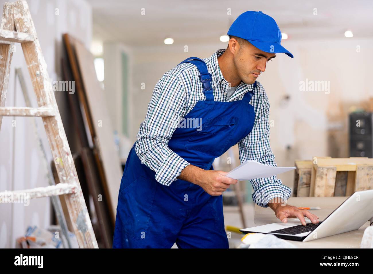 Man engineer che controlla i documenti e utilizza il computer portatile durante gli interventi di riparazione Foto Stock