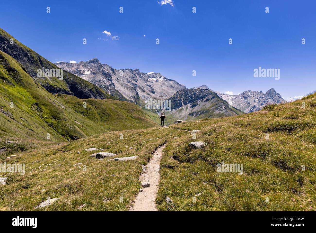 Vista di un paesaggio alpino molto grande e maestoso in stile Signore degli anelli. In primo piano una ragazza cammina verso le alte montagne sullo sfondo, che dominano la scena. Foto di alta qualità. Foto Stock