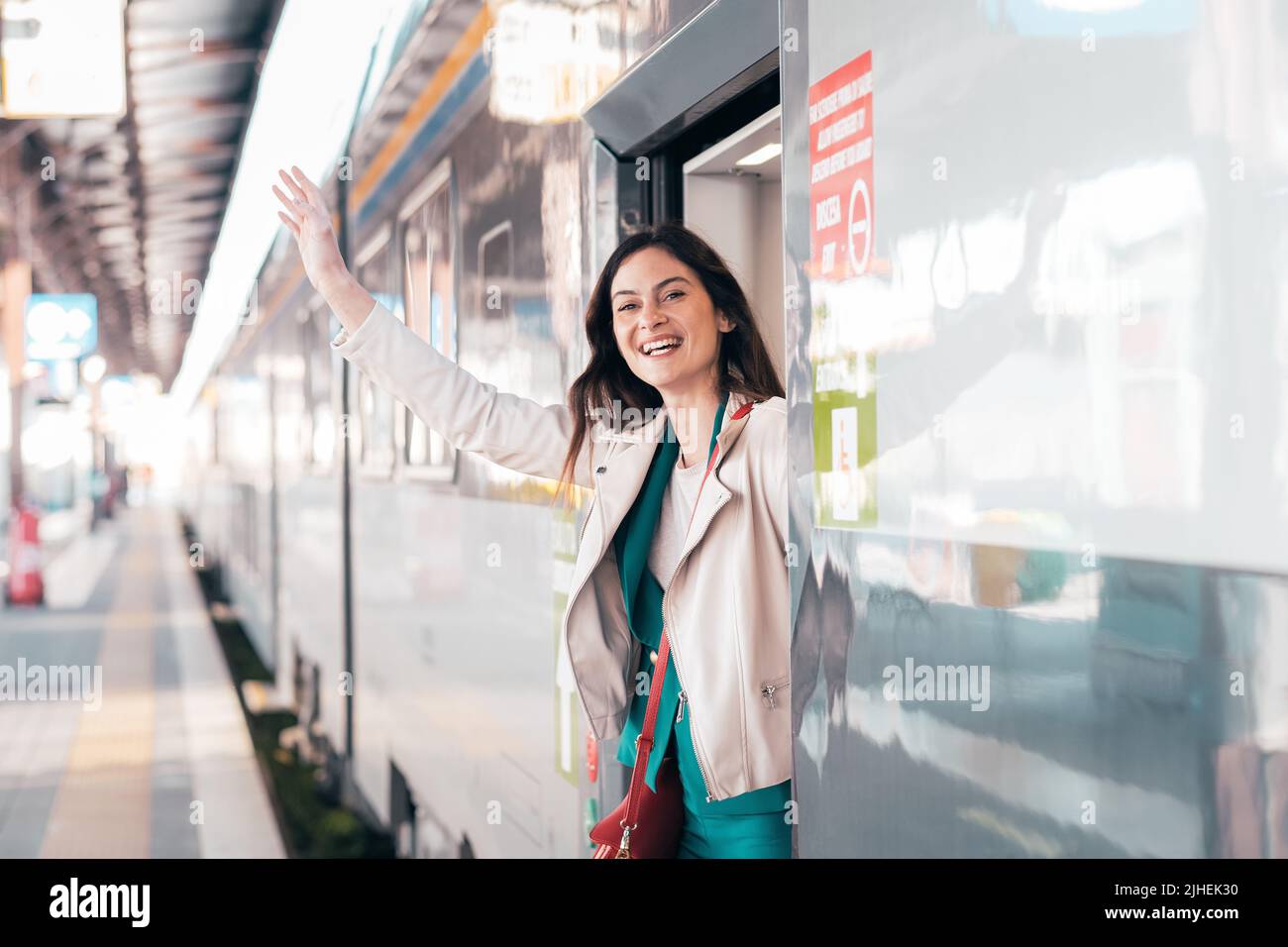 Potrait di bella donna del viaggiatore che esce dal treno sorridente - giovane donna di affari che sbirciava da una porta del treno che cerca qualcuno Foto Stock