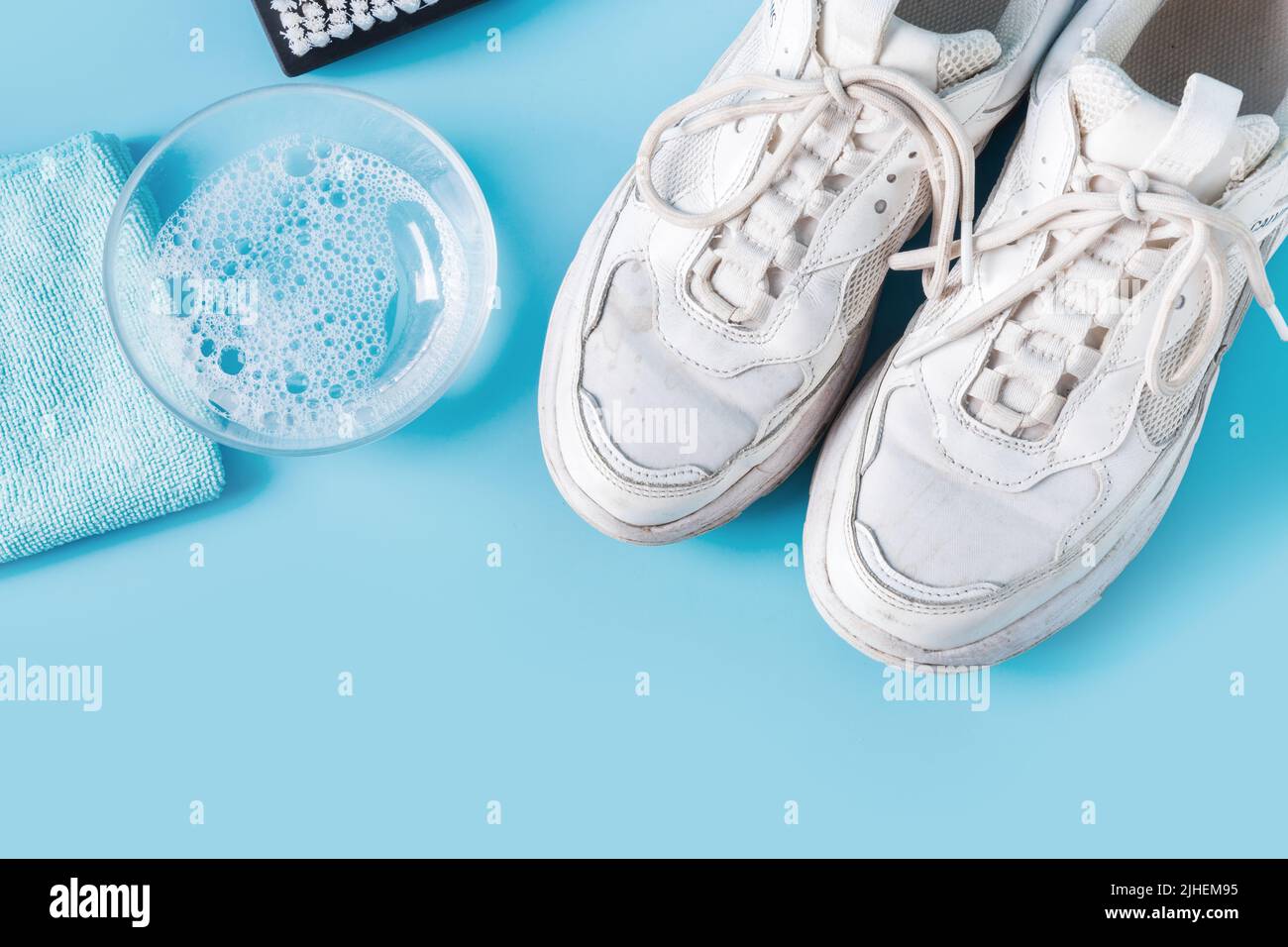 Sneakers bianche sporche con l'attrezzo speciale per pulirle su blu. Foto Stock