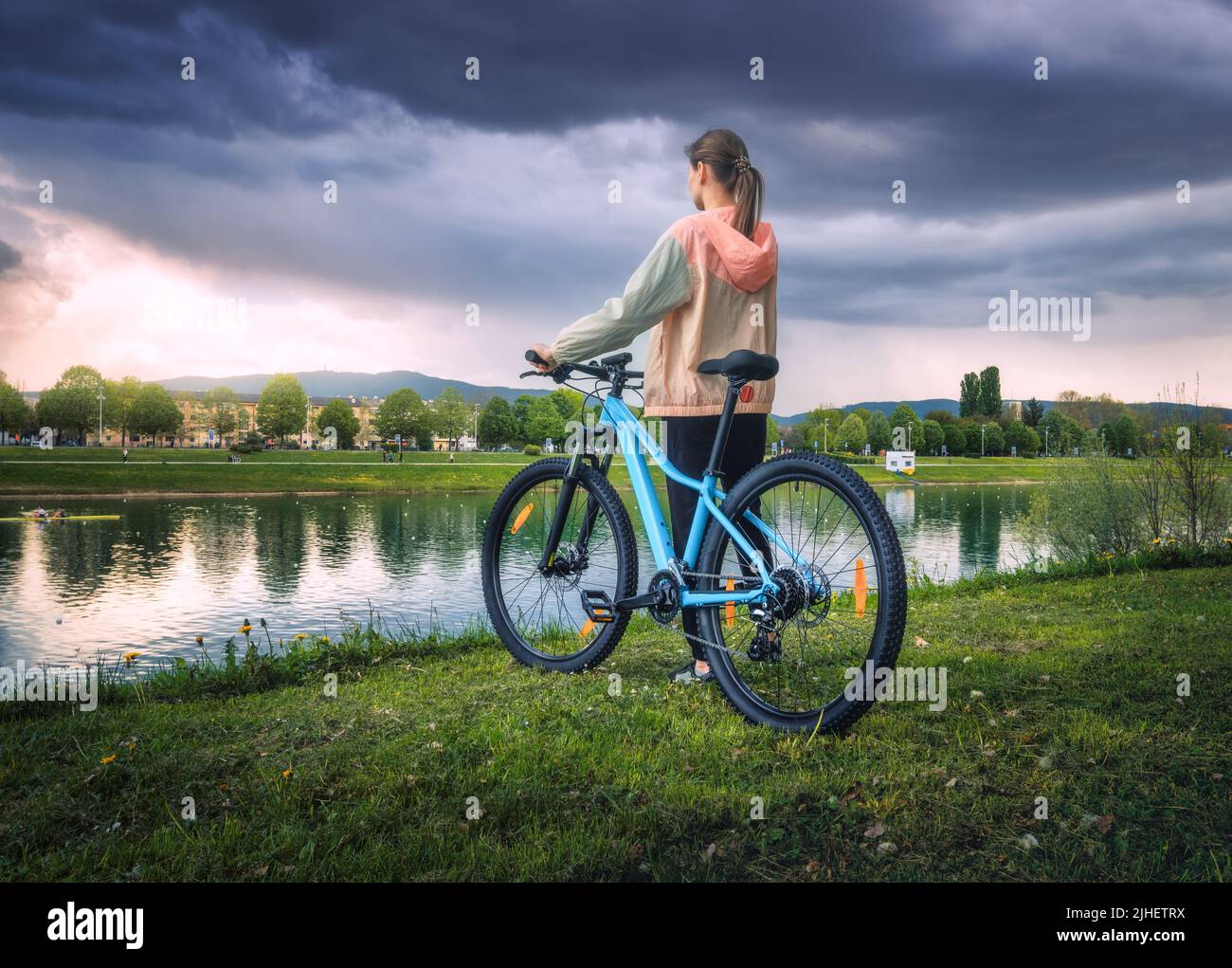 Donna che guida una mountain bike vicino al lago e cielo sovrastato in sprin Foto Stock