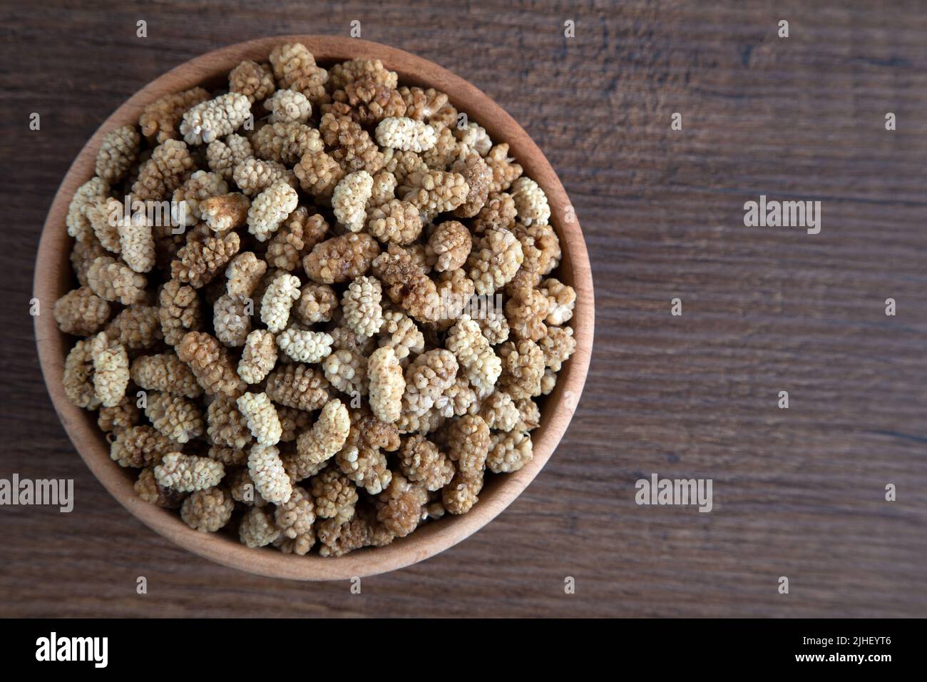 Ciotola piena di gelso secco su sfondo di legno Foto Stock