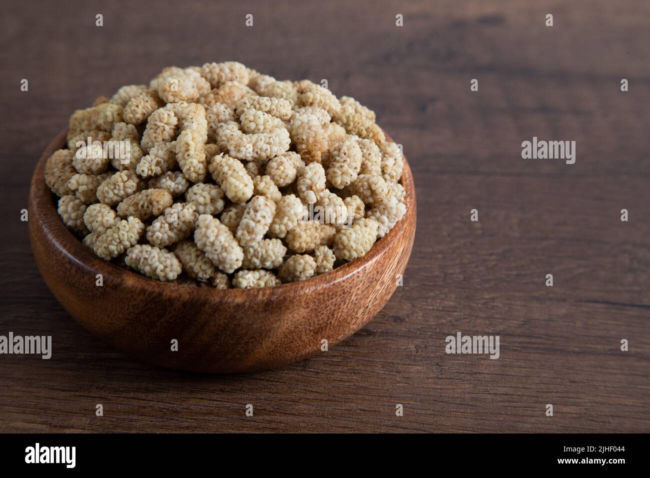 Ciotola piena di gelso secco su sfondo di legno Foto Stock