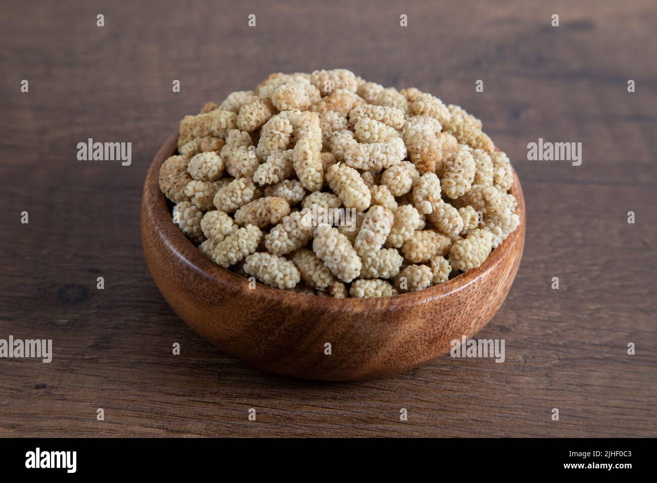 Ciotola piena di gelso secco su sfondo di legno Foto Stock