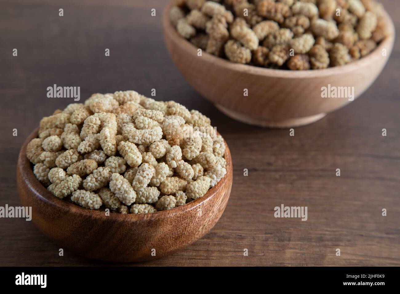 Ciotola piena di gelso secco su sfondo di legno Foto Stock