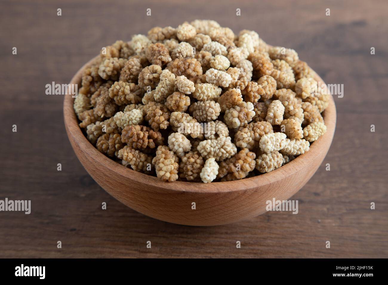 Ciotola piena di gelso secco su sfondo di legno Foto Stock