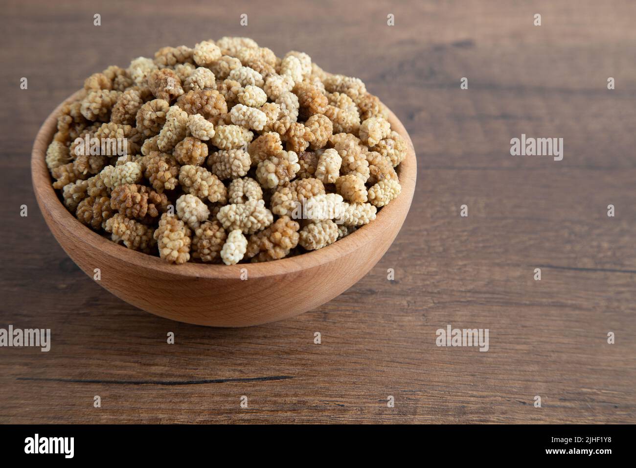 Ciotola piena di gelso secco su sfondo di legno Foto Stock