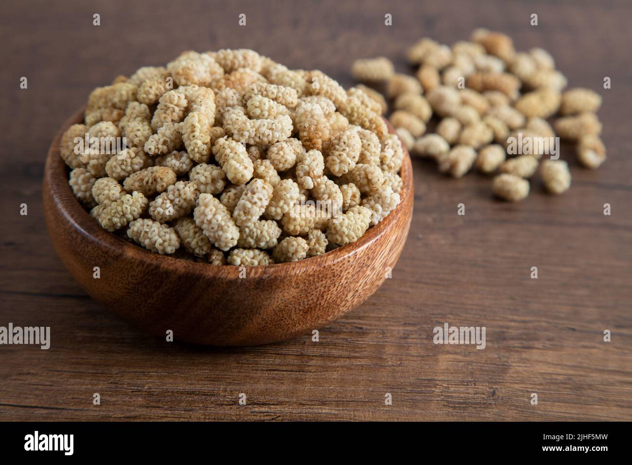 Ciotola piena di gelso secco su sfondo di legno Foto Stock