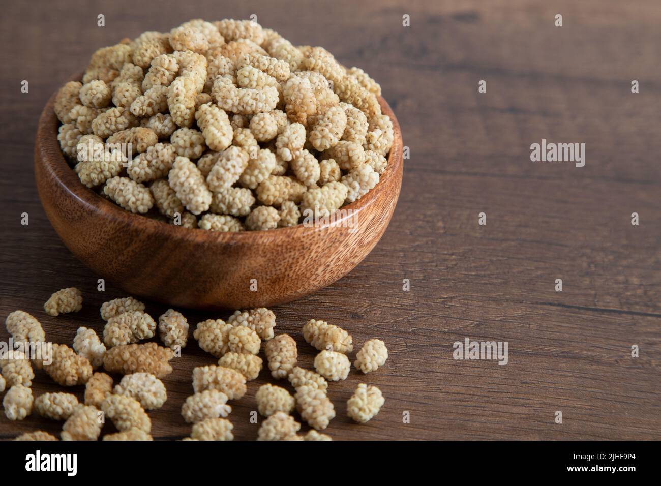 Ciotola piena di gelso secco su sfondo di legno Foto Stock