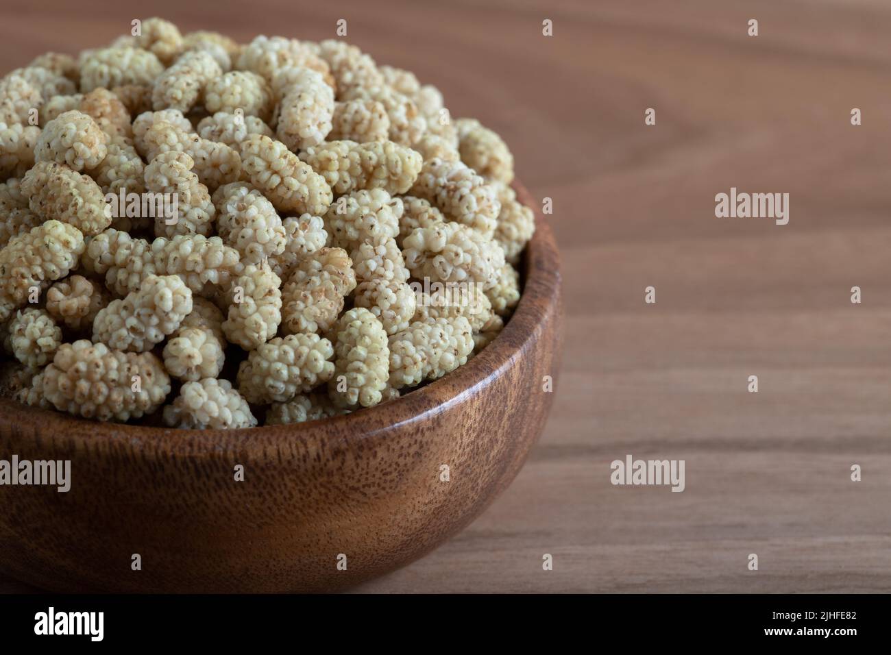 Ciotola piena di gelso secco su sfondo di legno Foto Stock
