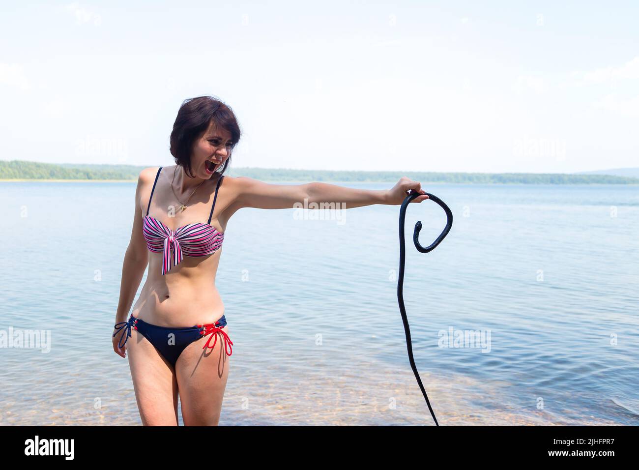 Donna spaventata urlando nella paura mentre tiene un serpente nelle sue mani, nuotando spiagge inverificate. Foto Stock