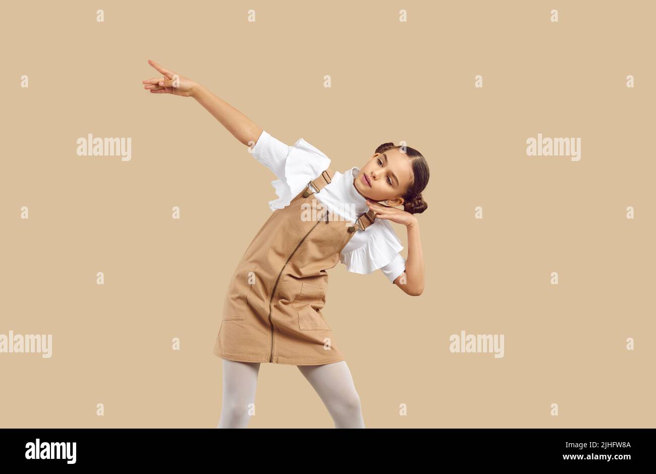 Piccola ragazza in denim beige casual vestito pinafore danza su sfondo beige studio Foto Stock