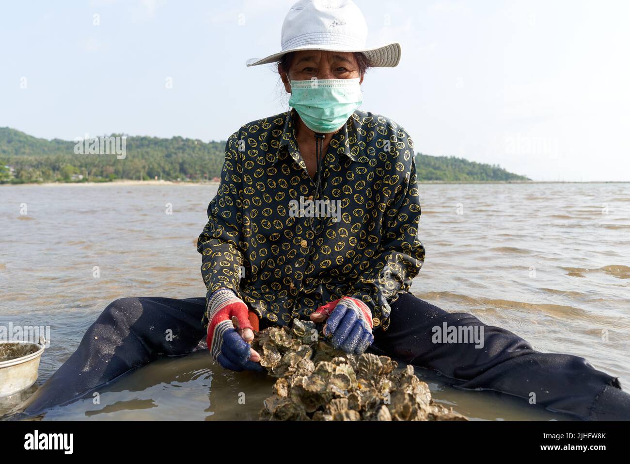 Ko Phangan, Thailandia, 15 marzo 2022: Donna anziana alla ricerca di vongole sul mare Foto Stock
