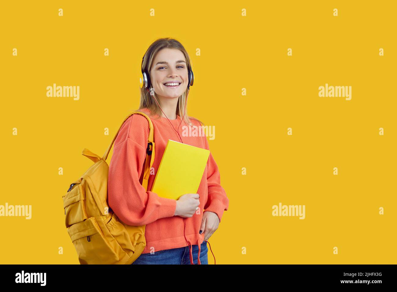Ritratto da studio di studente universitario felice e sorridente con libro, zaino e cuffie Foto Stock