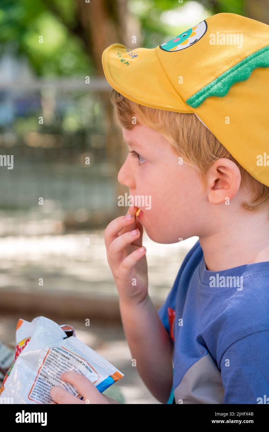 Il ragazzino carino che mangia patatine nel parco Foto Stock