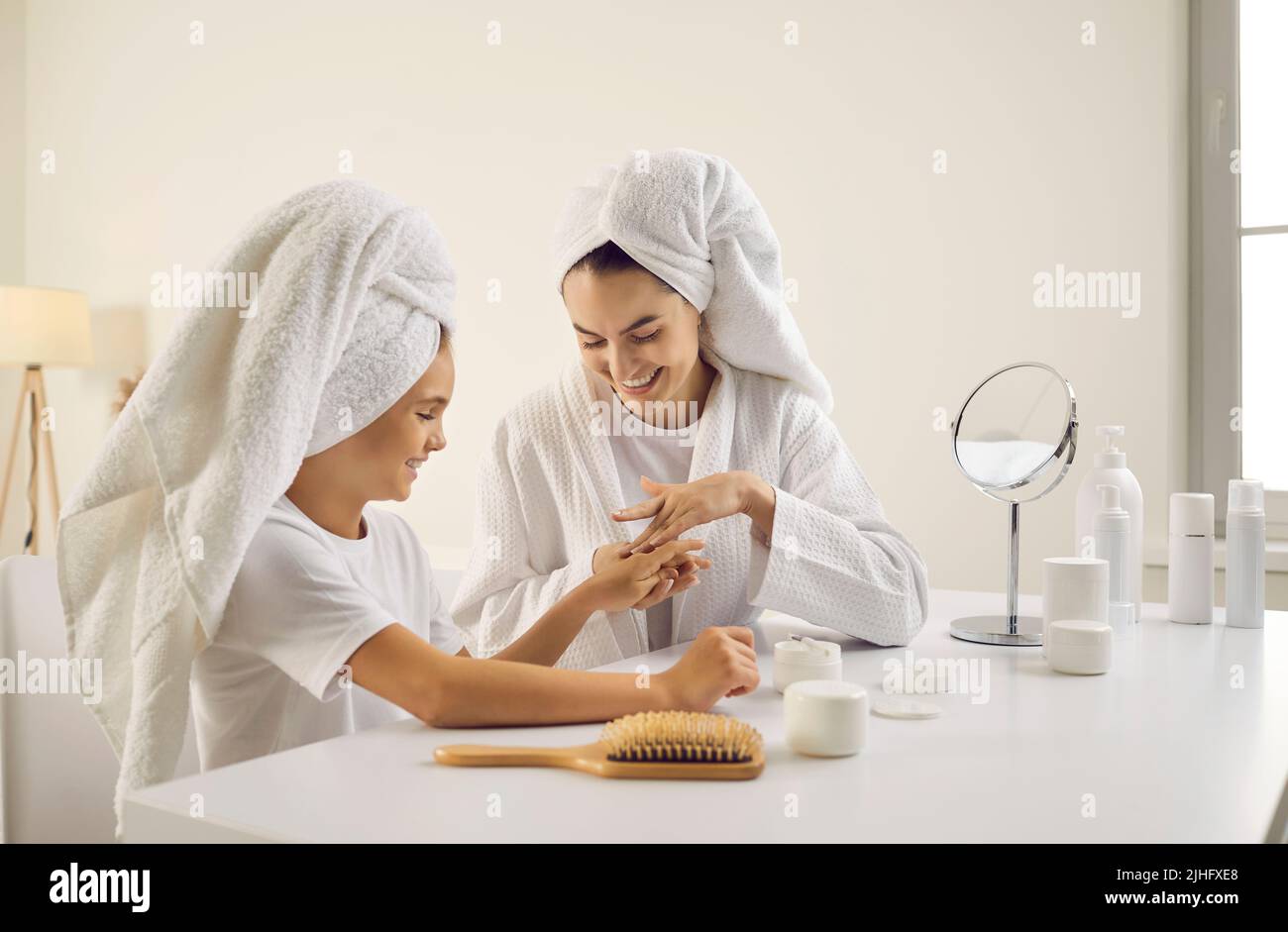 Madre felice e figlia che fanno la procedura di cura della pelle e applicando la crema della mano insieme Foto Stock