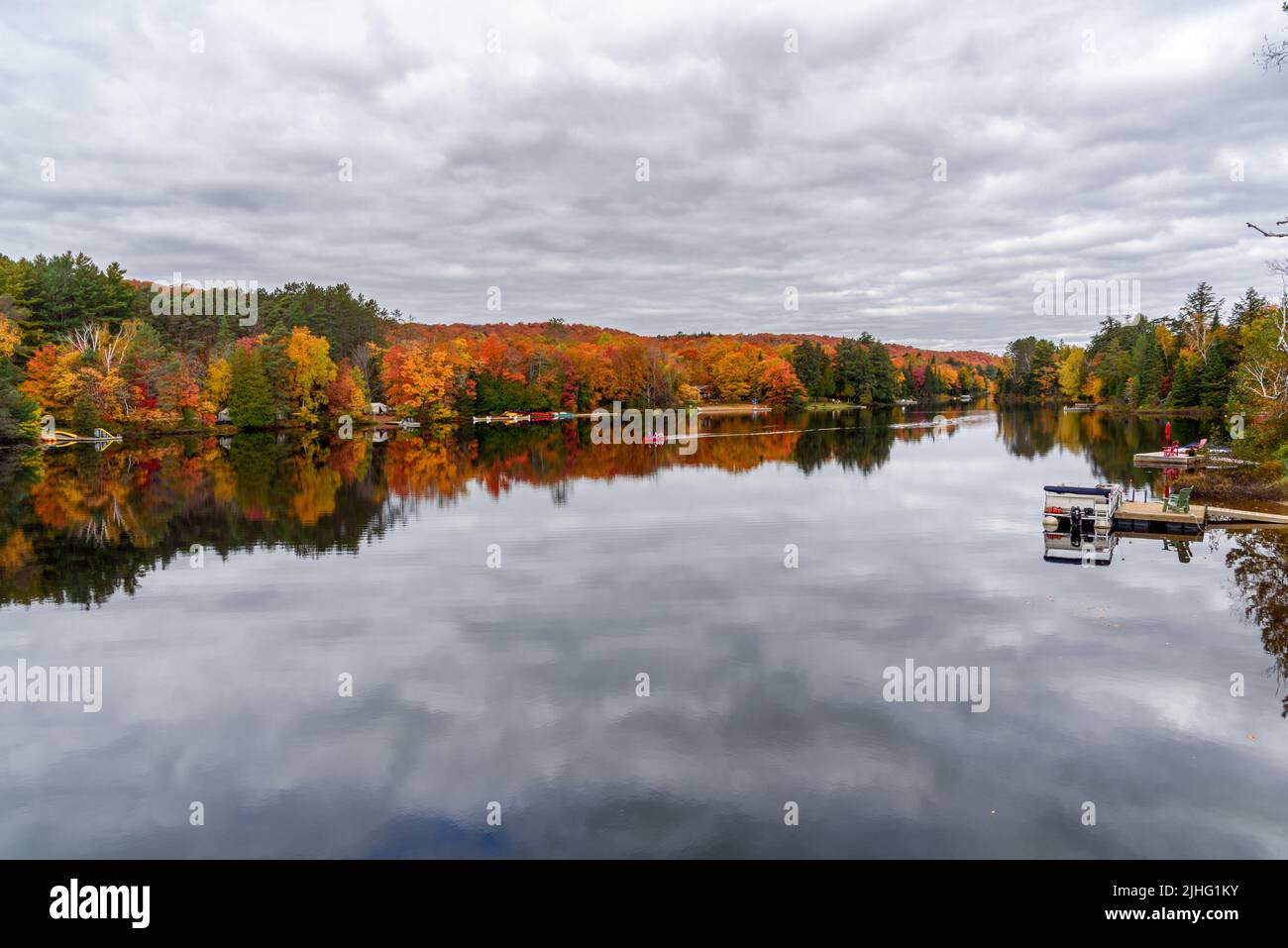 Bellissimo lago circondato da una foresta al picco del fogliame in autunno nuvoloso giorno d'autunno. La gente in canoa si trova al centro del lago. Foto Stock