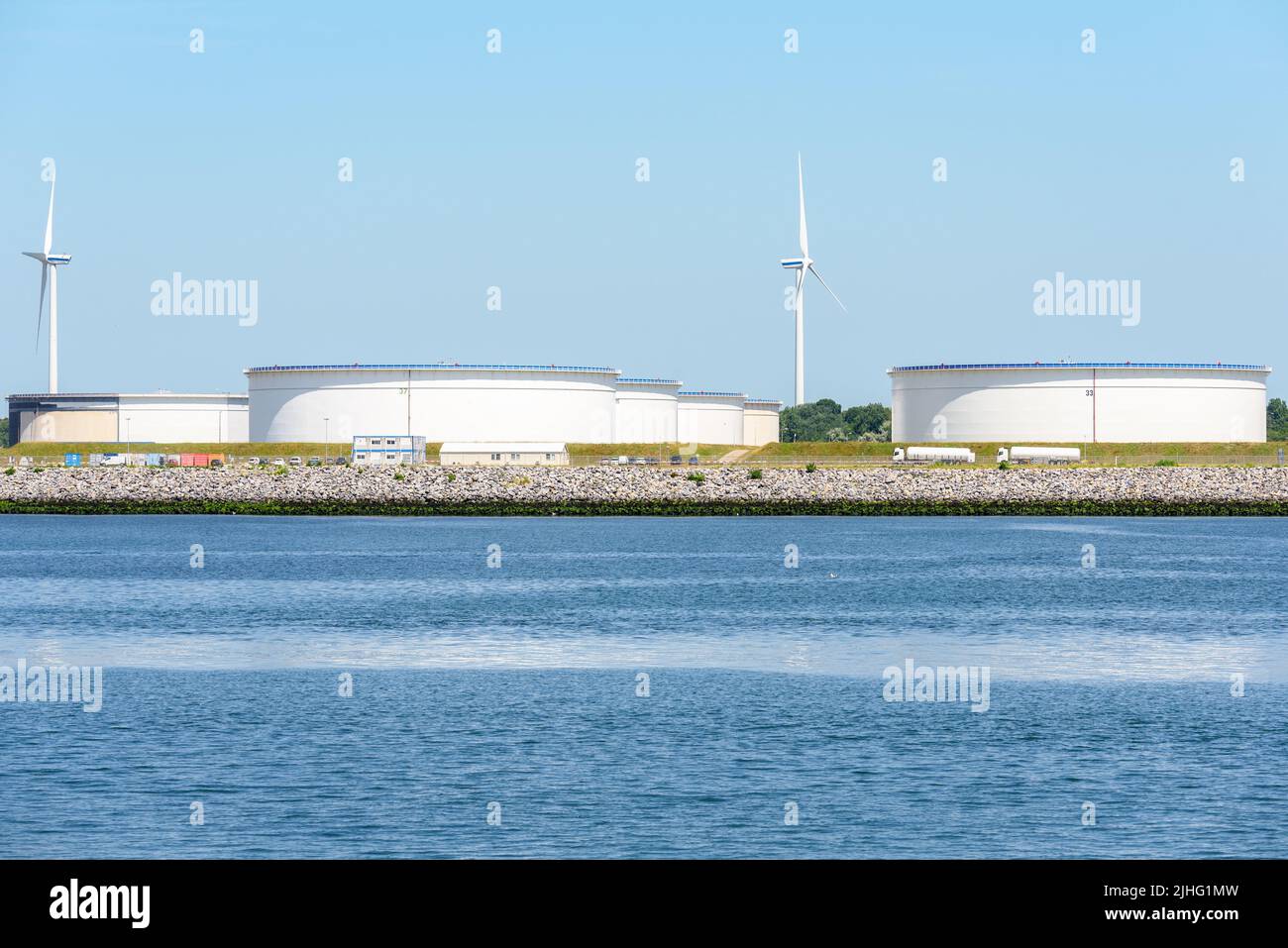 Grandi serbatoi d'olio in un porto in una giornata estiva soleggiata. Le turbine eoliche sono sullo sfondo. Foto Stock