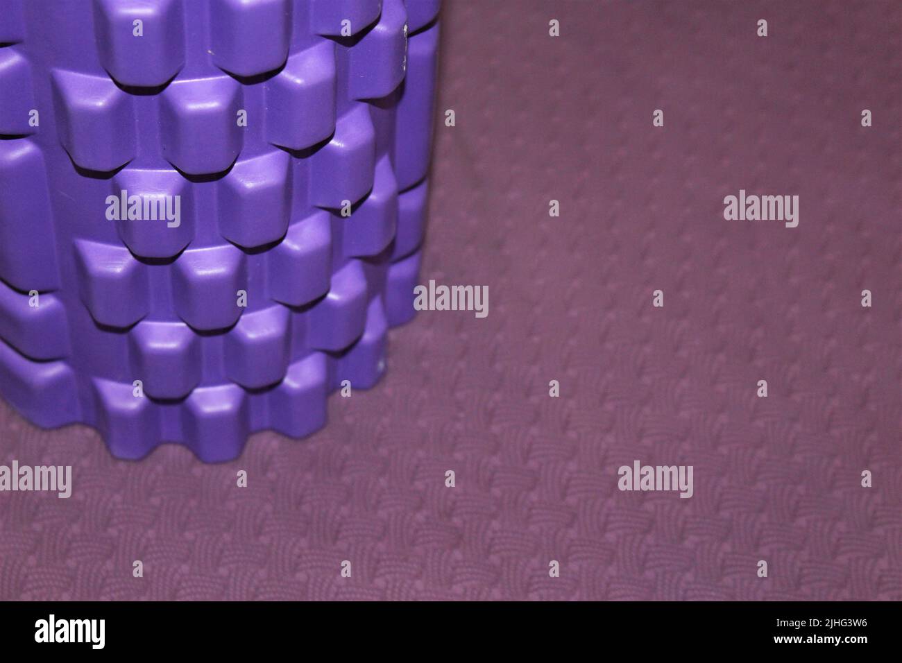 Rullo in schiuma viola su tappetino yoga mauve fondo di allenamento con spazio copia Foto Stock