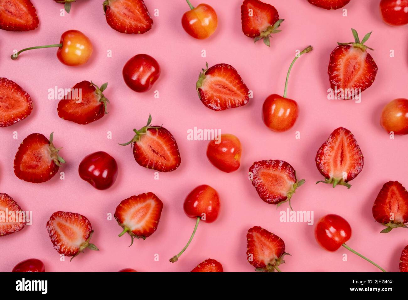 Sfondo di fragole e ciliegie mature su sfondo rosa.trendy, fruttato, sfondo estivo. Foto Stock