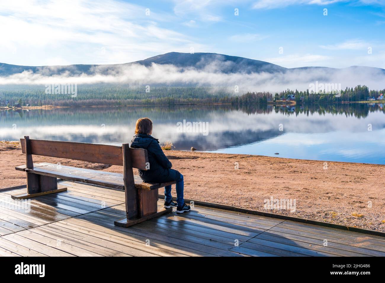 Donna seduta su una panchina in una spiaggia guardando la bella vista con montagna e fiume, Gällivare, Lapponia svedese, Svezia Foto Stock