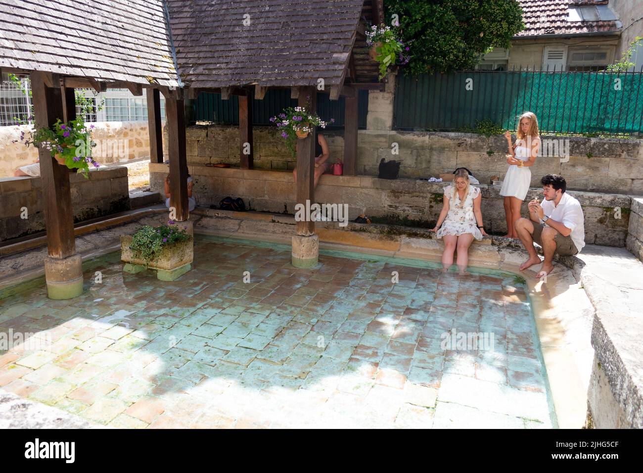 Persone che si raffreddano seduti con i piedi in acqua al lavatoio, in Rue de la Petite de la Fontaine Saint Emilion Francia Foto Stock