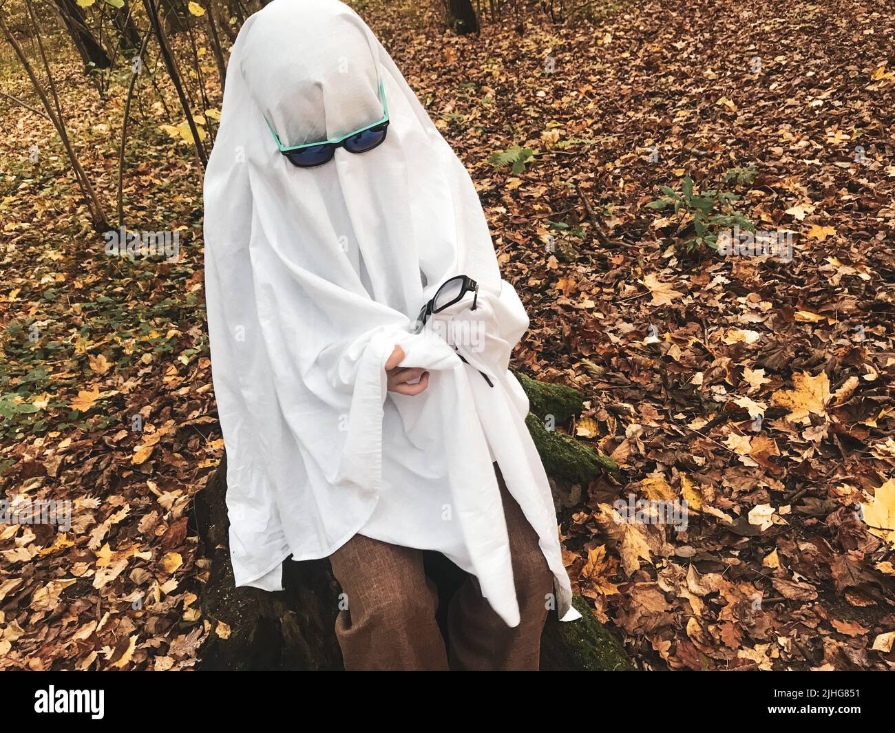 Un fantasma solitario nella foresta autunnale, in un foglio bianco con occhiali da sole, pulisce i vetri neri di un altro fantasma. Sfida fantasma Halloween. Foto Stock