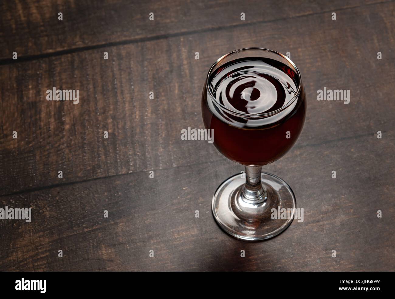 Gocce di vino e onde che si formano in un bicchiere pieno di vino rosso in piedi su un tavolo di legno Foto Stock