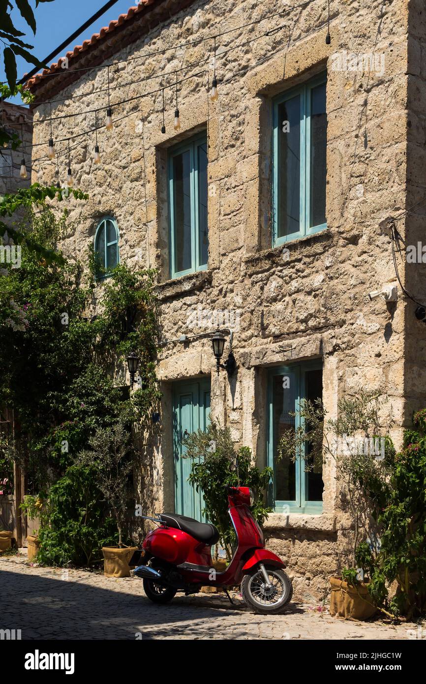 Vista di una moto rossa, alberi e vecchie case storiche in pietra tradizionale nella famosa città turistica del mar Egeo chiamata Alacati. È un villaggio di Cesm Foto Stock