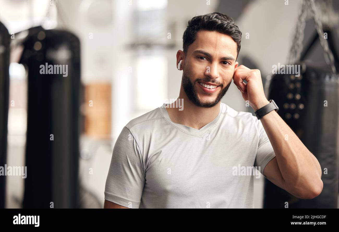 Ritratto di un giovane ispanico sicuro che ascolta la musica con auricolari wireless bluetooth per rimanere motivato mentre si esercita in palestra. Felice Foto Stock