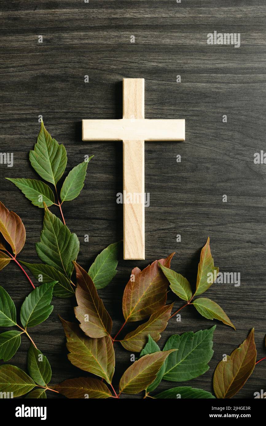 Piccola croce cristiana su sfondo di legno scuro con un bordo di foglie autunnali mutevoli in rosso e verde con spazio copia Foto Stock