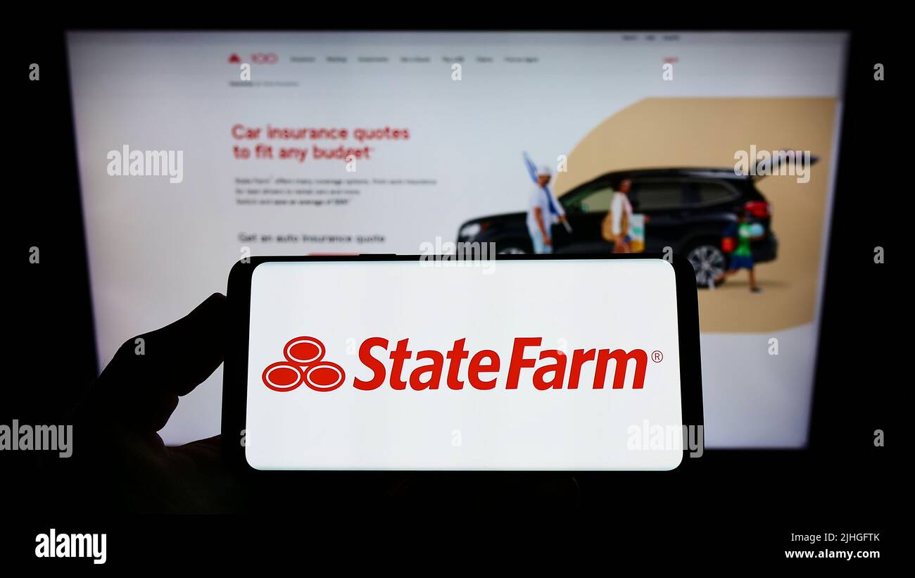 Persona che tiene lo smartphone con il logo della state Farm Mutual Automobile Insurance Company sullo schermo di fronte al sito Web. Mettere a fuoco sul display del telefono. Foto Stock