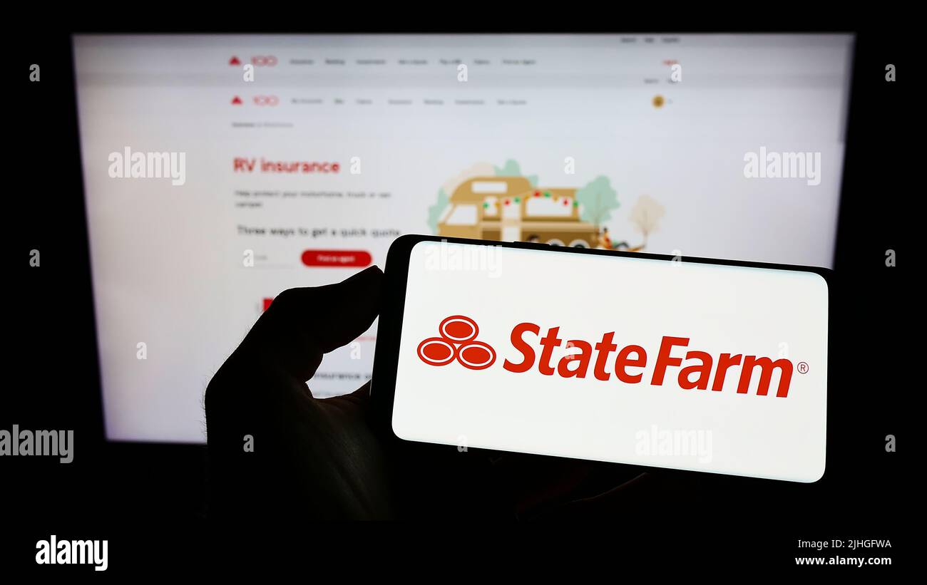 Persona che tiene il cellulare con il logo della US state Farm Mutual Automobile Insurance Company sullo schermo di fronte alla pagina web. Mettere a fuoco sul display del telefono. Foto Stock