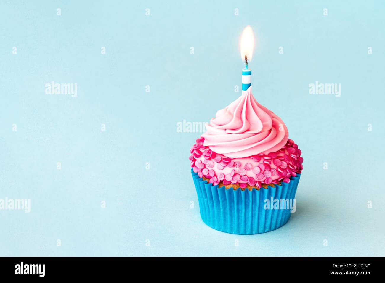 Cupcake di compleanno con candela di compleanno a righe e spolverini rosa su sfondo blu Foto Stock