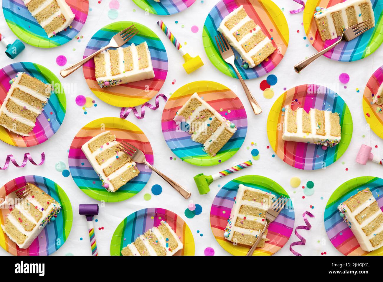 Sfondo colorato della festa di compleanno con fette di torta di compleanno su piatti colorati dell'arcobaleno durante una festa di compleanno Foto Stock