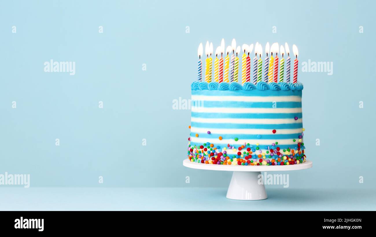 Torta di compleanno a strisce con candele di compleanno colorate e spolverate su sfondo blu Foto Stock