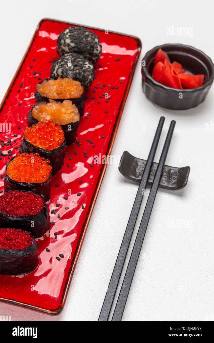 Set di sushi su piatto rosso. Zenzero rosa in recipiente nero. Bastoni di cibo. Vista dall'alto. Sfondo bianco Foto Stock