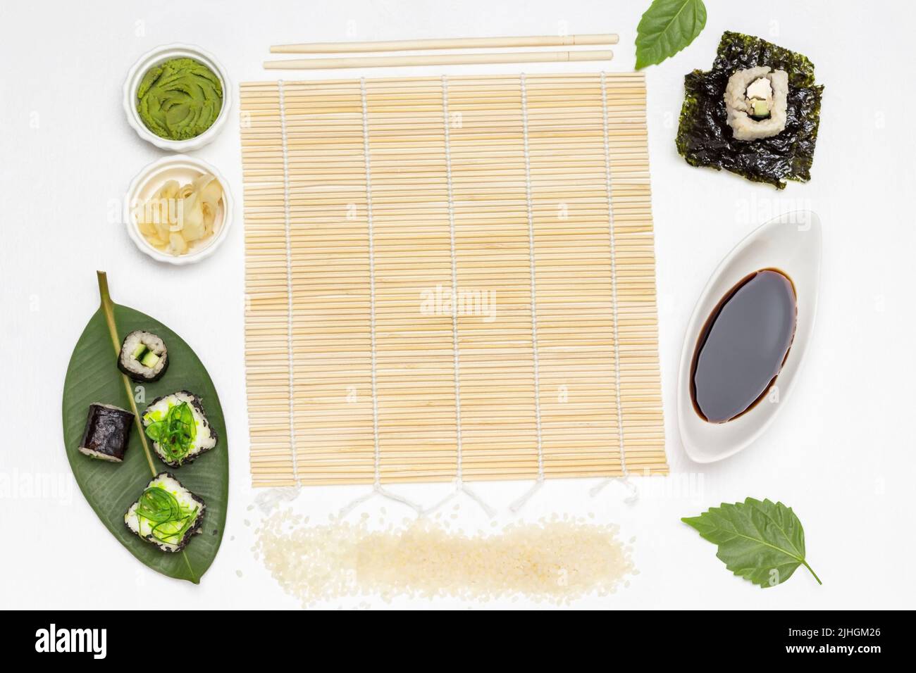Processo di preparazione del sushi piatto. Stuoia di bambù, riso, salsa di soia e foglie di nori. Sfondo bianco Foto Stock