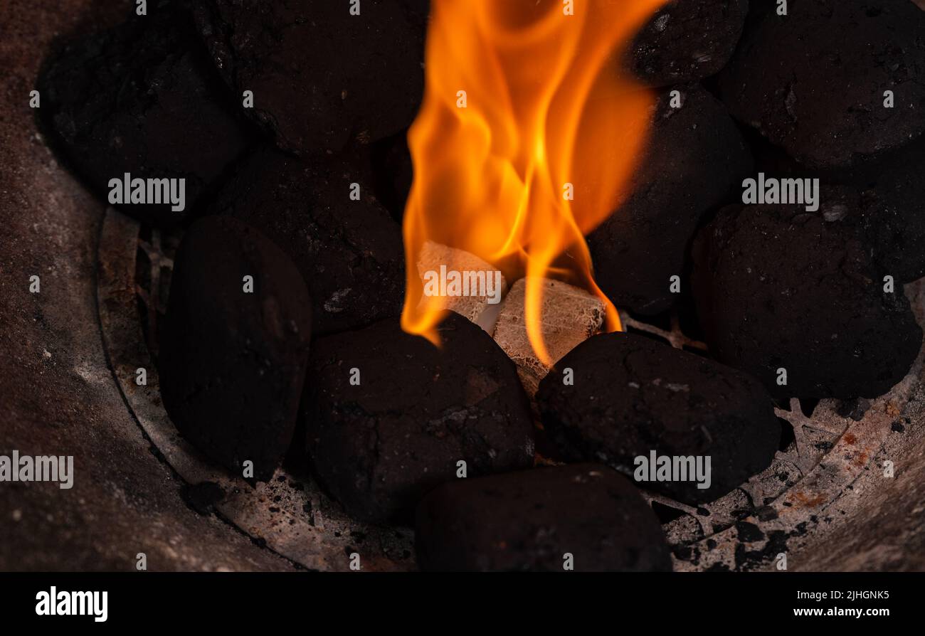 Illuminazione di un barbecue fuoco. Accendino a legna e cubo bianco alla griglia. Fiamma con carbone. Foto Stock