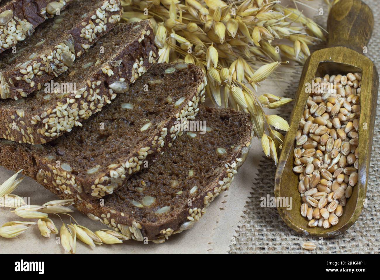 Pane nero con semi di sesamo e semi di girasole, pikelets di avena e grani di grano in un cucchiaio di legno Foto Stock