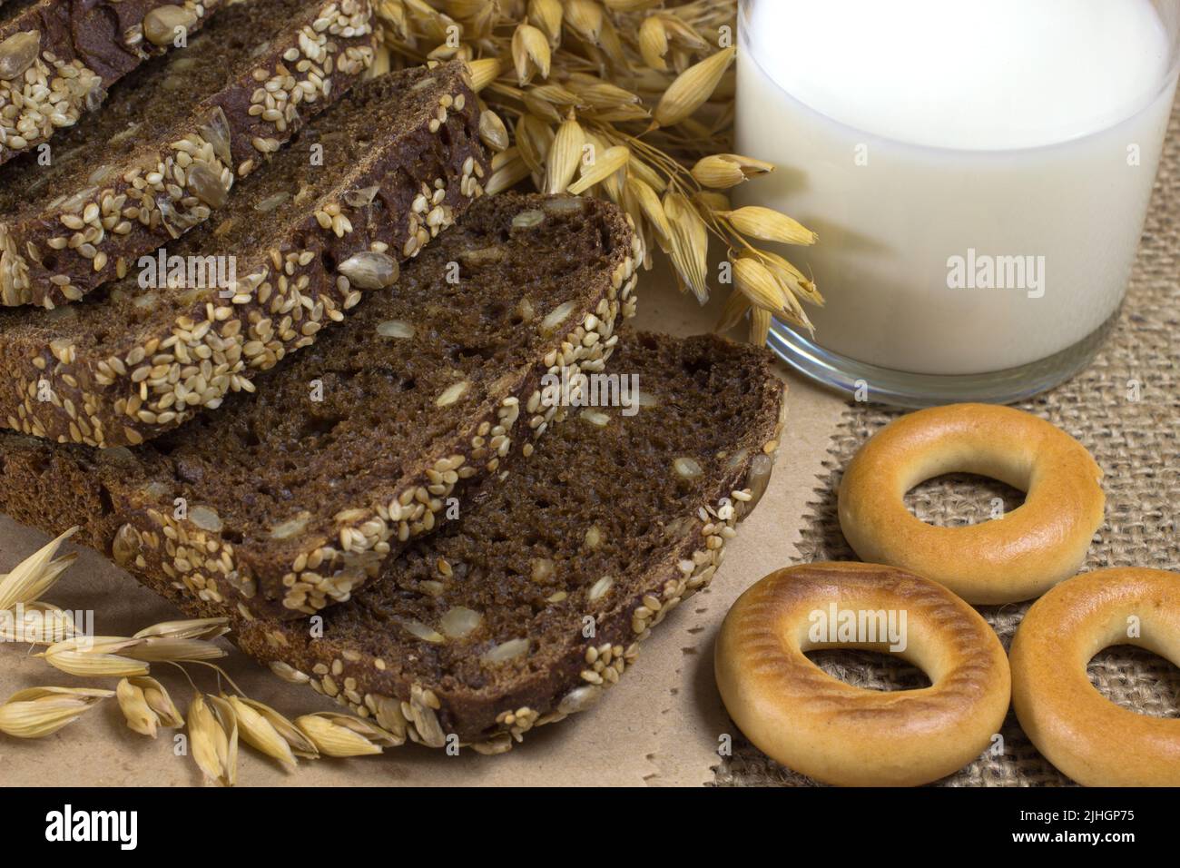 Pane nero con semi di sesamo e semi di girasole, avena, spighe di grano, un bicchiere di latte Foto Stock